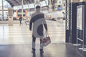 Confident adult man standing with travel bag at the hall of railway station and looking his train.