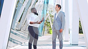 Confident African-American businessman and his colleague in front of modern office building. Financial investors are