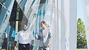 Confident African-American businessman and his colleague in front of modern office building. Financial investors are