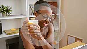 Confident african american businesswoman enjoys morning coffee break in office, beaming with the joy of success