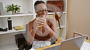Confident african american businesswoman joyfully working success-driven laptop job, drinking morning coffee in office interior,