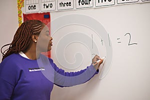 Confident African American female math teacher writing numbers on the whiteboard in the classroom