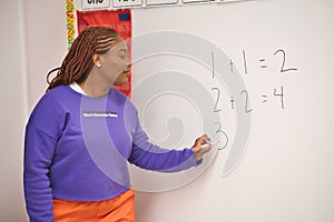 Confident African American female math teacher writing 
 numbers on the whiteboard in the classroom