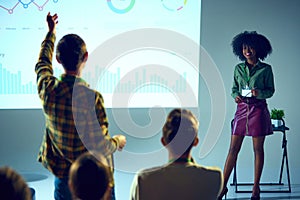 Confident African-American woman, expert with stands in front of audience, giving lecture and answer questions in