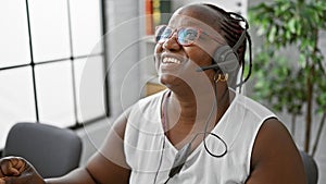 Confident african american woman happily working as a business executive, wearing a headset, and smiling at the office, speaking