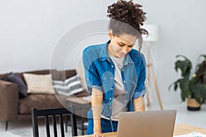 Confident African American woman standing in modern office and working using laptop online