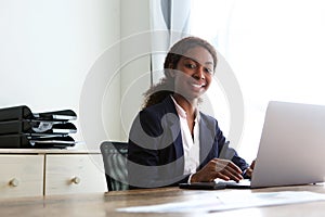 Confident african businesswoman sitting at desk with laptop