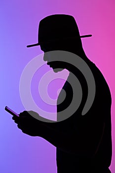 Confident african man silhouette using mobile phone while standing to neon background