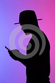 Confident african man silhouette using mobile phone while standing to neon background