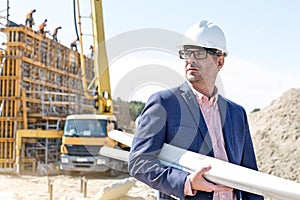 Confident architect holding rolled up blueprints at construction site