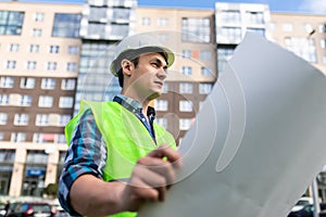 Confident architect holding rolled up blueprints at construction site outdoors