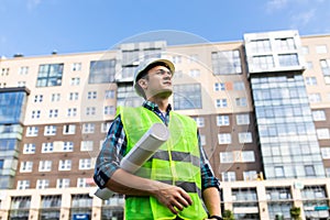 Confident architect holding rolled up blueprints at construction site outdoors