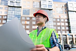 Confident architect holding rolled up blueprints at construction site outdoors