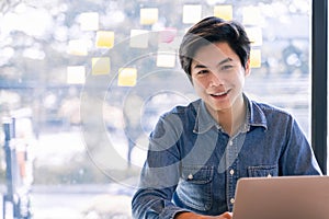 Confident asian business male smiling and look at camera while working on laptop computer at office