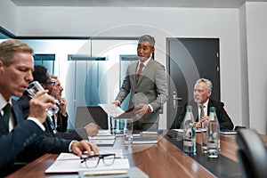 Confident asian businessman in formal wear holding some document and discussing project results with multicultural team