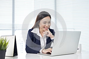 Confident asian businesswoman sitting by desk with laptop in off