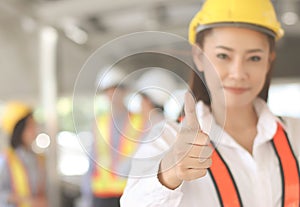 Confident Asian Female architect or engineer  holding blue print paper, standing in front of her team smiling , looking at camera