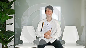 Confident Asian male candidate sits in a waiting room, waiting for his job interview