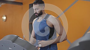 Confident athletic man running on treadmill in sports club. Portrait of young handsome Middle Eastern sportsman keeping