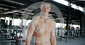 Confident athletic man standing at gym, rest from workout and looking at camera