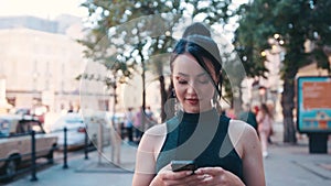 Confident attractive blue-eyed brunette woman in a stylish outfit walks down the central cityâ€™s street, uses her phone