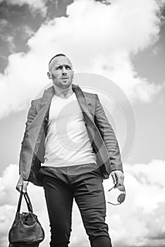 Confident attractive man waiting for his transport wearing a white T-shirt, brown jacket, and comfortable pants