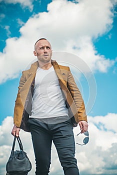 Confident attractive man waiting for his transport wearing a white T-shirt, brown jacket, and comfortable pants against