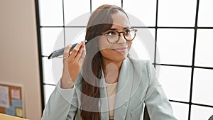 Confident and attractive young hispanic business woman eagerly listens to a voice message on her smartphone while working