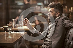Confident bar customer speak in cafe. Date or business meeting of hipster in pub. Bearded man in restaurant.