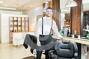 Confident Barber Smiling While Standing By Chair In Shop