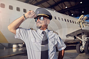 Confident bearded male holding pilots hat on the head while sending time in the outdoors