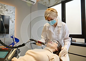 Confident beautician aesthetician performs cosmetic procedures on a woman`s face using a modal laser to remove age and age spots