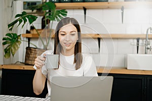 Confident beautiful Asian businesswoman typing laptop computer and digital tablet while holding coffee at home