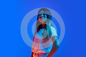 Confident, beautiful Asian woman, business lady posing looking at camera against blue gradient background in neon light.