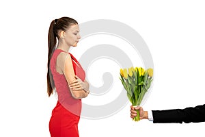 Confident beautiful serious brunette girl in red dress stands with crosed hands and looking at yellow tulips in male