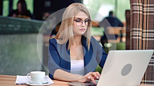 Confident beautiful young business female working in cafe looking at screen of laptop