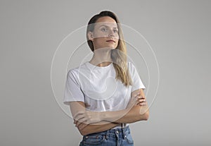 Confident beautiful young european woman with arms crossed, white t-shirt, looking aside and up, successful woman posing studio