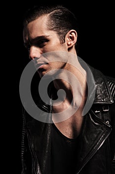 Confident biker in leather jacket posing in dark studio