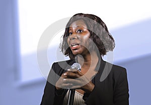 Confident black African American business woman with microphone speaking in auditorium at corporate event or seminar giving