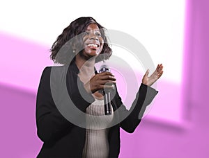 Confident black afro American business woman with microphone speaking in auditorium at corporate event or seminar giving