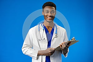 Confident black doctor posing over blue studio background.