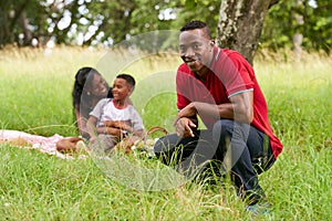 Confident Black Man Smiling At Camera And Family Doing Picnic