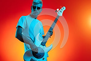 Confident blonde hipster man crush white bass guitar in neon lights. Rock music concept.