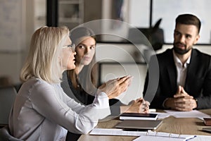 Confident blonde senior business professional woman talking to younger colleagues