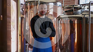 Confident brewer crossing hands looking at camera standing in brewery indoors. Portrait of young handsome unshaved