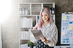 Confident business expert attractive smiling young woman typing laptop ang holding digital tablet on desk in creative office