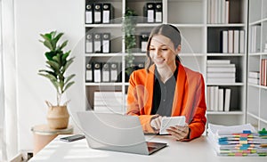 Confident business expert attractive smiling young woman typing laptop ang holding digital tablet on desk in office