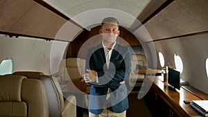 Confident business man with crossed arms inside of private jet seriously looking at you
