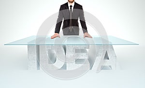 Confident business man leaning on empty glass table with a base made of concrete IDEA table. Business concept