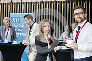 Confident business people holding coffee cups at lobby in convention center